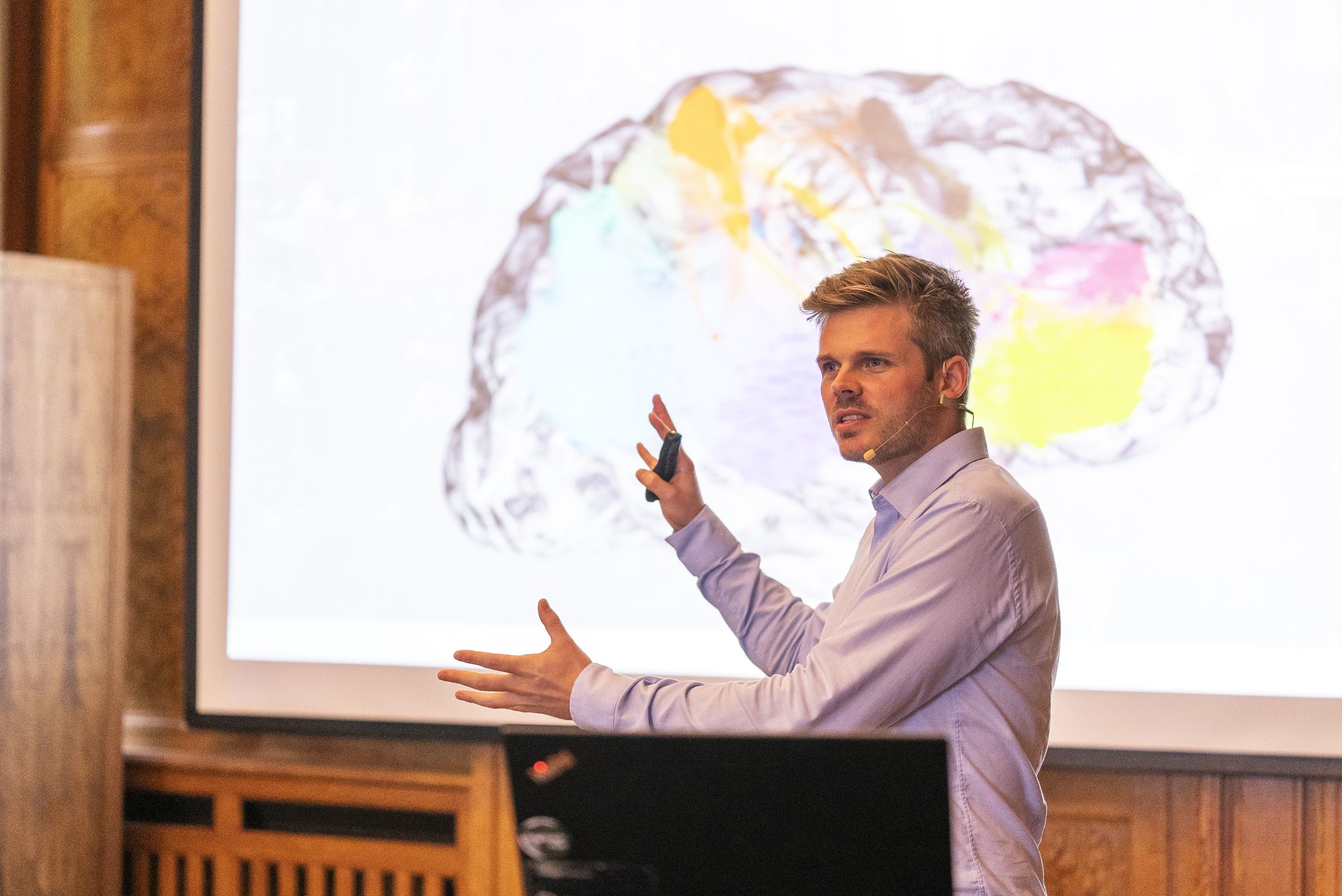 Dr. Jonathan T. Mall erklärt auf der IAA-Bühne in einer hellen Halle eine Gehirn-Visualisierung neben einer großen Präsentationsfolie