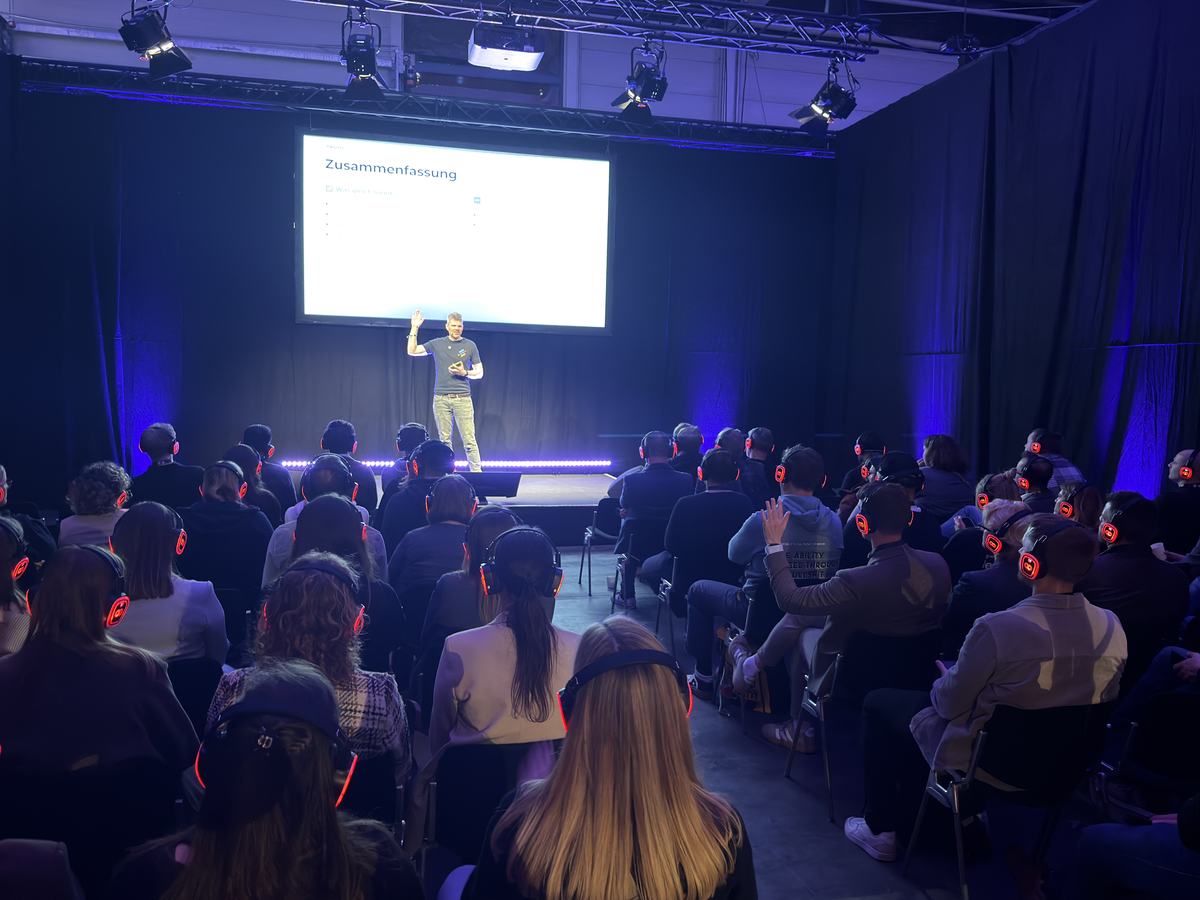 Dr. Jonathan Mall im B&uuml;hnenlicht vor Publikum mit leuchtenden Silent-Conference-Kopfh&ouml;rern